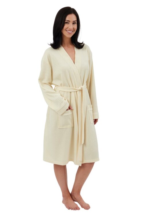 A woman in a cream-colored waffle-knit robe stands with a smile on a white background. 